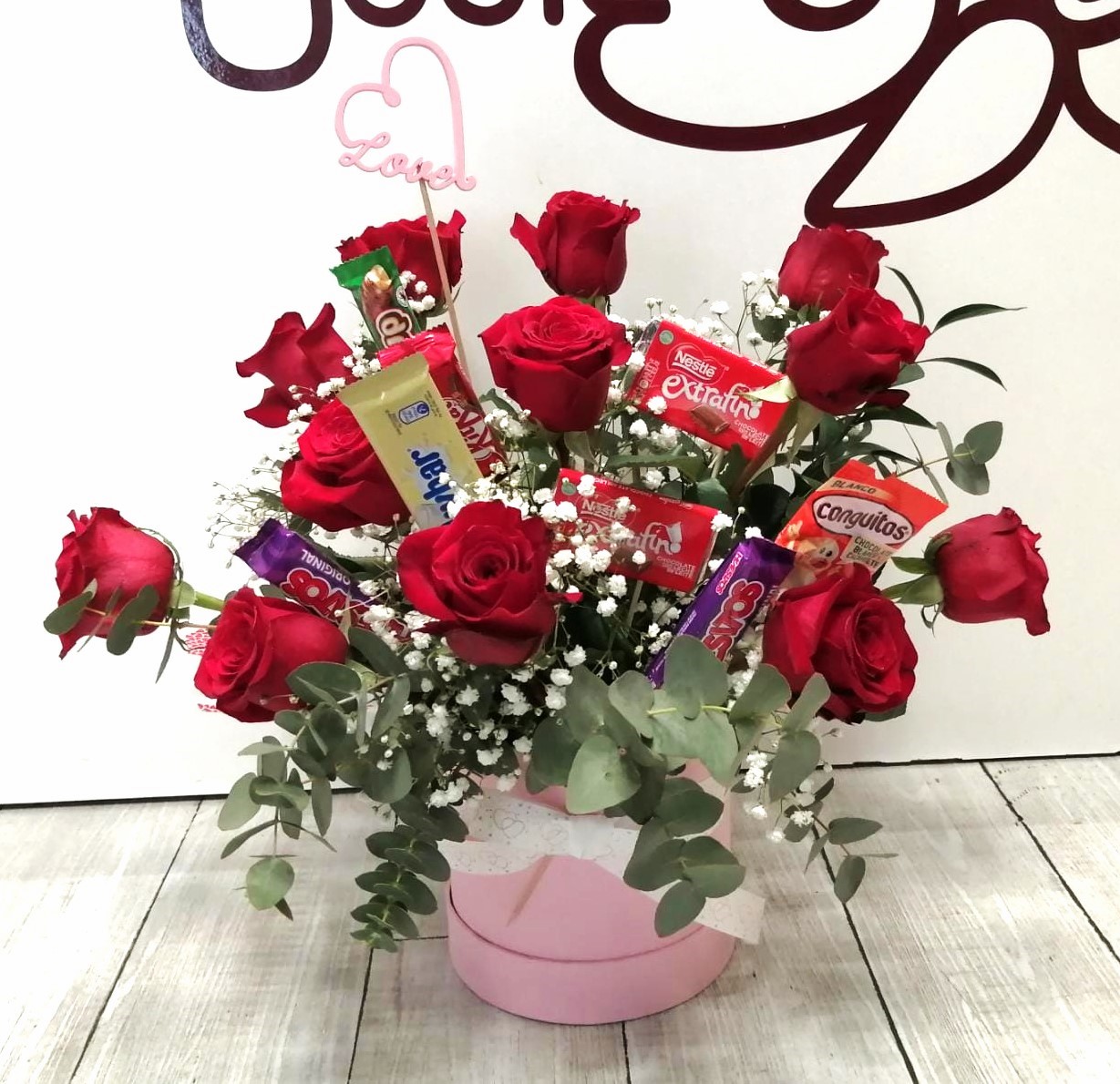 Caja de 12 rosas naturales en color rojo con chocolatinas surtidas y decoración